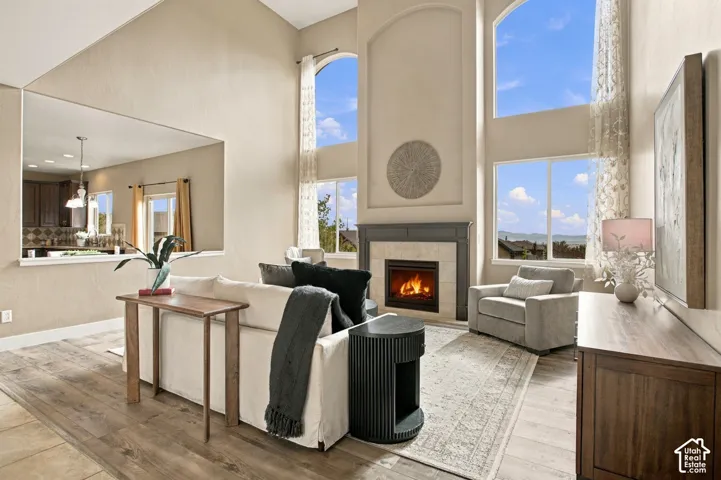 Vaulted ceilings featuring expansive windows, wood-finish flooring, and a fireplace with a stone-surround mantle