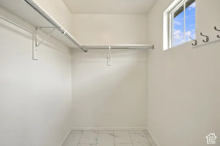 Walk-in storage area featuring light-toned tile flooring, built-in metal shelving, a natural light window, and wall-mounted garment hooks