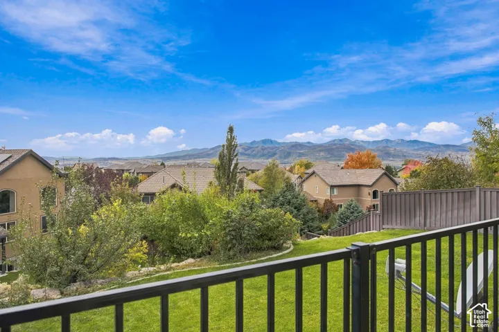 Exterior space featuring a metal railing, grass-covered yard, privacy fencing, and a mountain range backdrop