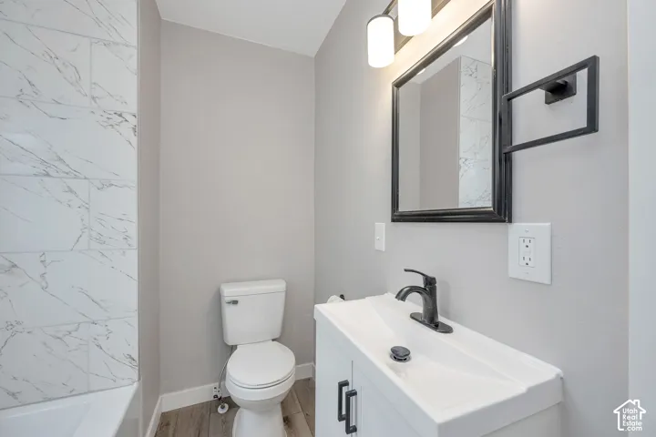 Bathroom featuring a white vanity cabinet with matte black hardware, a high-arc faucet, wall-mounted light fixture with glass shades, and white tile wall surround with grey veining