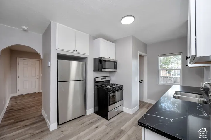 Kitchen featuring dark stone-patterned countertops, stainless steel appliances, white cabinetry, wood-finish flooring, and an arched doorway