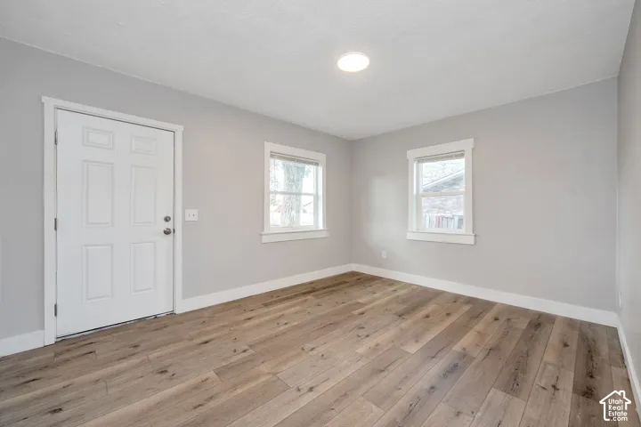 Interior space featuring neutral wall paint, wood-finish flooring, two multi-pane windows with white trim, and a six-panel entry door