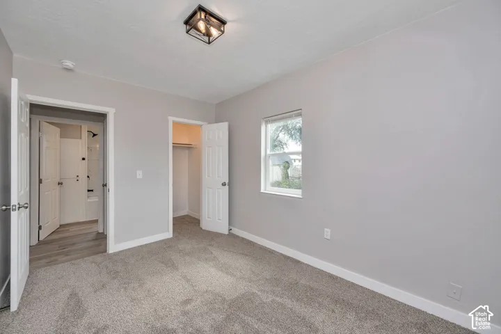 Neutral-toned interior featuring wall-to-wall carpeting, a multi-paneled closet door, a single-light window, and a ceiling-mounted geometric light fixture
