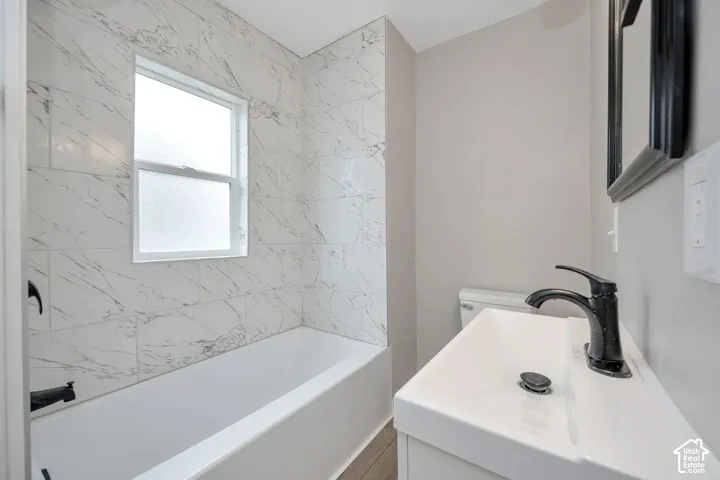 Bathroom featuring a white bathtub with full-height stone-patterned tile surround, white vanity, and matte black plumbing fixtures