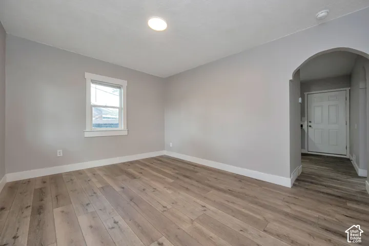 Neutral-toned interior space featuring wood-finish flooring, a single-pane window with traditional casing, and a distinctive arched architectural opening