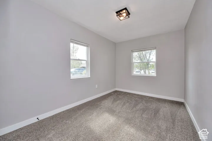 Neutral-toned interior space featuring neutral wall paint, wall-to-wall carpeting, dual windows, and a flush-mount ceiling light fixture