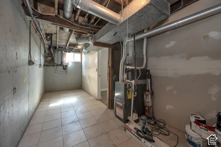 Utility area featuring ceramic tile flooring, exposed ceiling joists, concrete foundation walls, and a dedicated furnace system