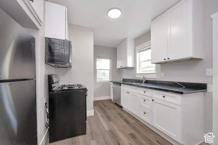 Kitchen featuring white shaker-style cabinetry, dark stone-finish countertops, wood-finish flooring, and stainless steel appliances