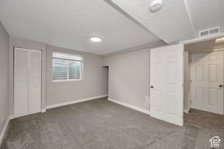 Neutral-toned interior space featuring wall-to-wall carpeting, white louvered closet doors, and recessed window with a corrugated metal window well