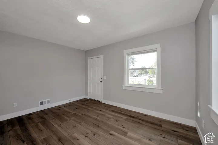 Neutral-toned interior room featuring wood-finish flooring, a six-panel door, and a single-hung window with white casing