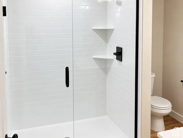Walk-in shower with white subway tile surround, integrated shelving, glass door, matte black hardware, and wood-finish flooring