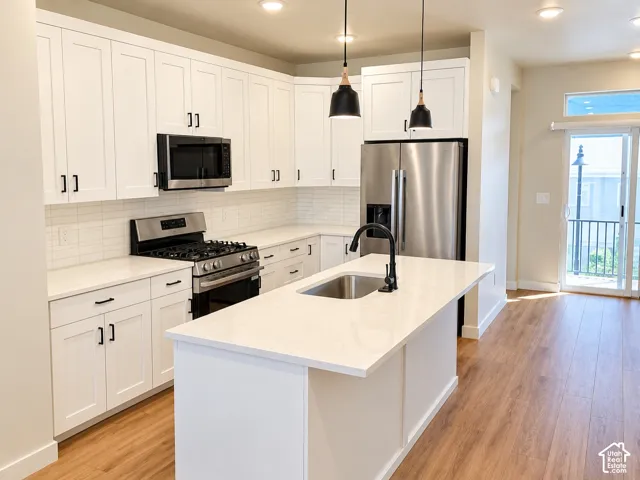 Kitchen featuring white cabinetry, solid-surface countertops, stainless steel appliances, a center island with an undermount sink, and wood-finish flooring