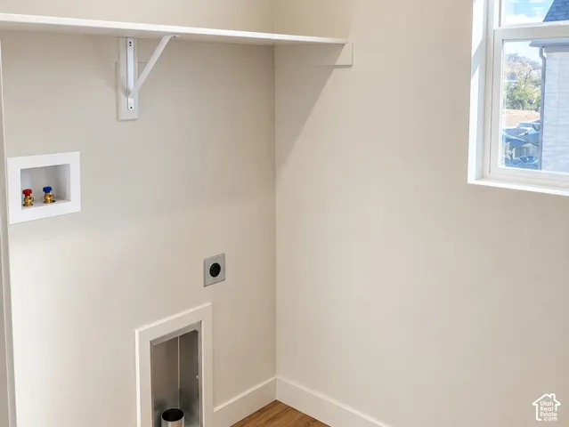 Utility space featuring wood-finish flooring, a wall-mounted shelving unit, and dedicated hookups for laundry appliances