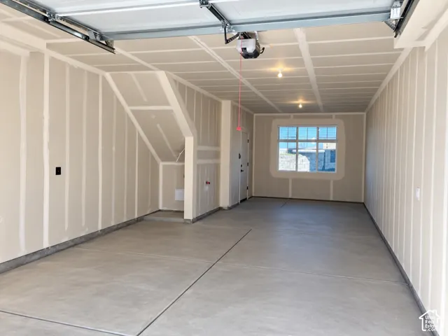 Finished interior garage featuring concrete flooring, drywall walls, ceiling-mounted automatic door opener, and a single-pane window