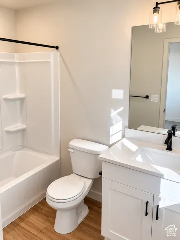 Bathroom featuring a vanity with a white countertop and rectangular undermount sink, matte black faucet, shaker-style cabinetry, wood-finish flooring, and a tub-shower combination with a black curtain rod