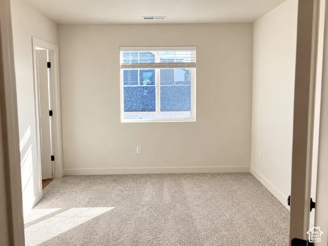 Neutral-toned interior featuring wall-to-wall carpeting, window with integrated blinds, and solid-core door with matte black hardware