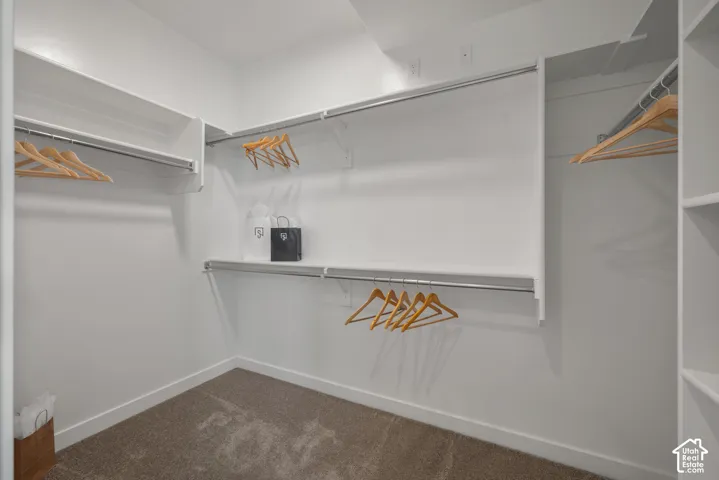 Walk-in closet featuring tiered white shelving, integrated metal clothing rods, and wall-to-wall carpeting
