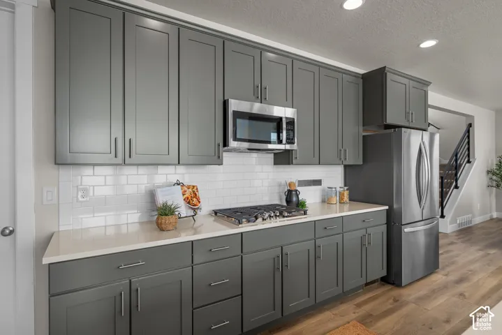 Kitchen featuring charcoal-finished shaker cabinetry, white subway tile backsplash, solid-surface countertops, stainless steel appliances, and wood-finish flooring