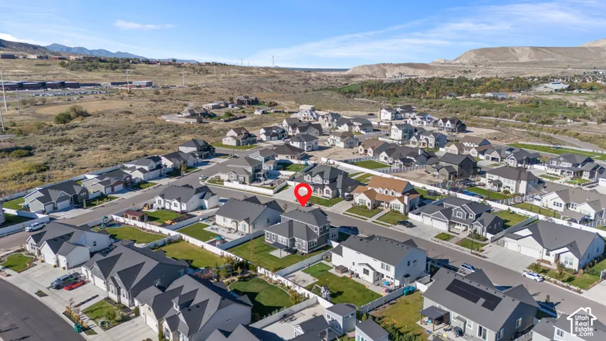 Aerial view of a residential property featuring a fenced backyard, multi-level roofline, concrete driveway, and surrounding mountainous terrain