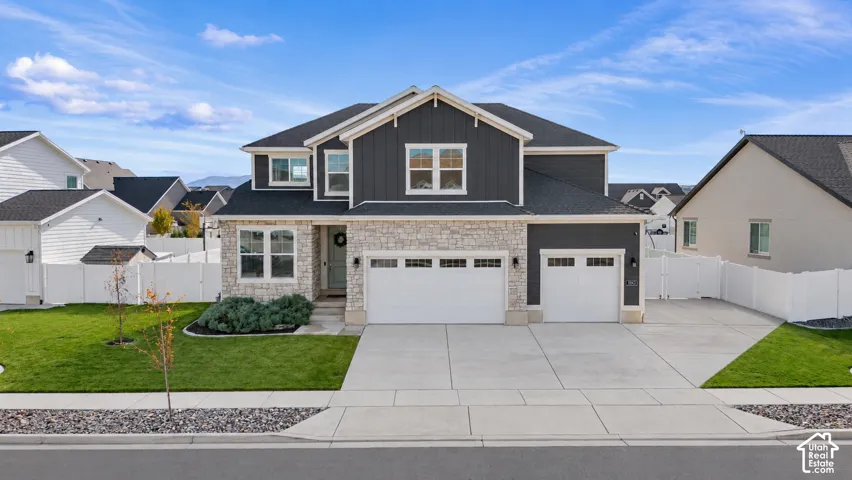 Two-story exterior featuring dark vertical siding, stone veneer accents, an asphalt shingle roof, three-car garage, and concrete driveway