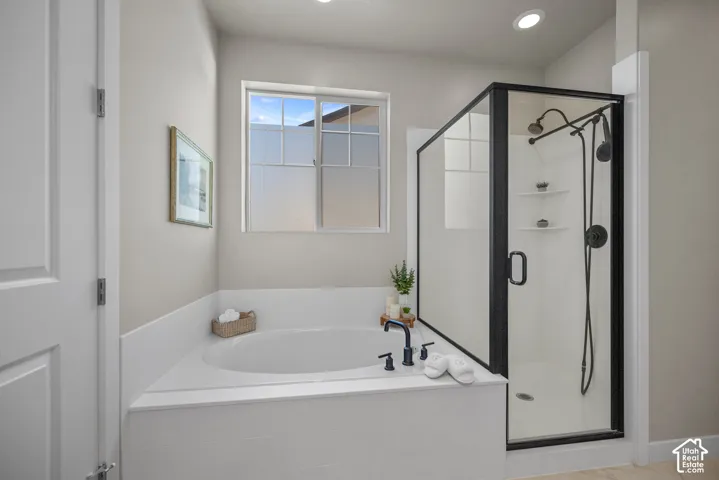 Soaking tub with matte black faucet, separate shower enclosure with matte black frame and matching rainfall showerhead, recessed lighting, and grid-pattern window
