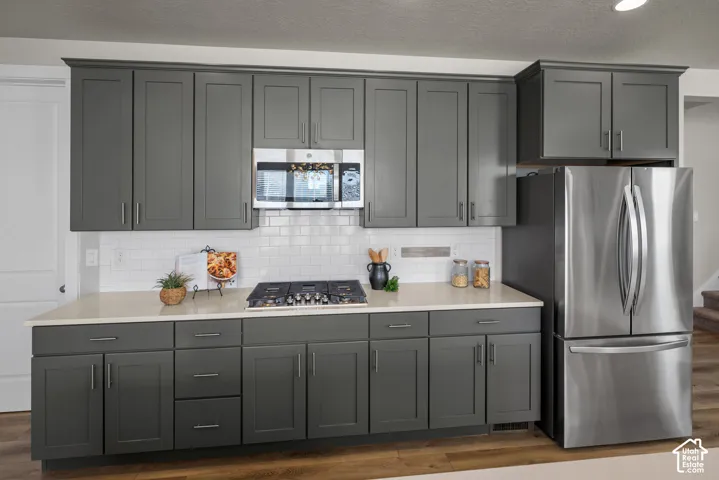 Kitchen featuring dark charcoal shaker-style cabinetry, quartz countertops, white subway tile backsplash, integrated stainless steel appliances, and wood-finish flooring