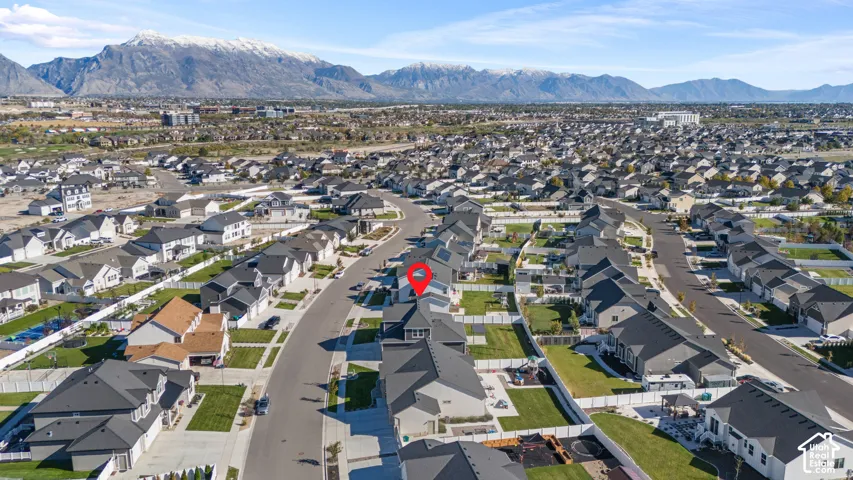 Aerial perspective of residential property featuring a fenced backyard, asphalt shingled roof, attached garage, and prominent mountain backdrop