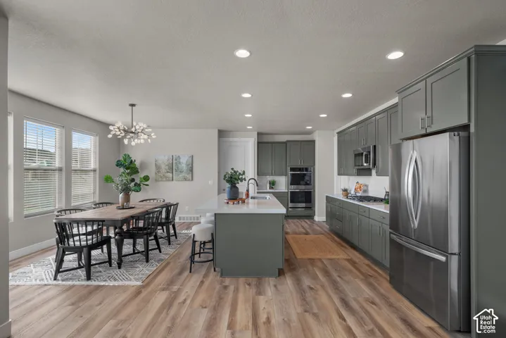 Kitchen featuring flat-panel cabinetry, quartz countertops, a central island with an integrated sink, built-in double wall ovens, and wood-finish flooring