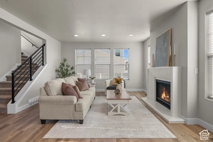 Living area featuring wood-finish flooring, recessed lighting, a fireplace with a minimalist surround, and a staircase with a black metal railing