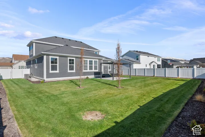 Rear exterior featuring horizontal lap siding, a concrete patio with a metal pergola, a fenced backyard, and professional landscaping