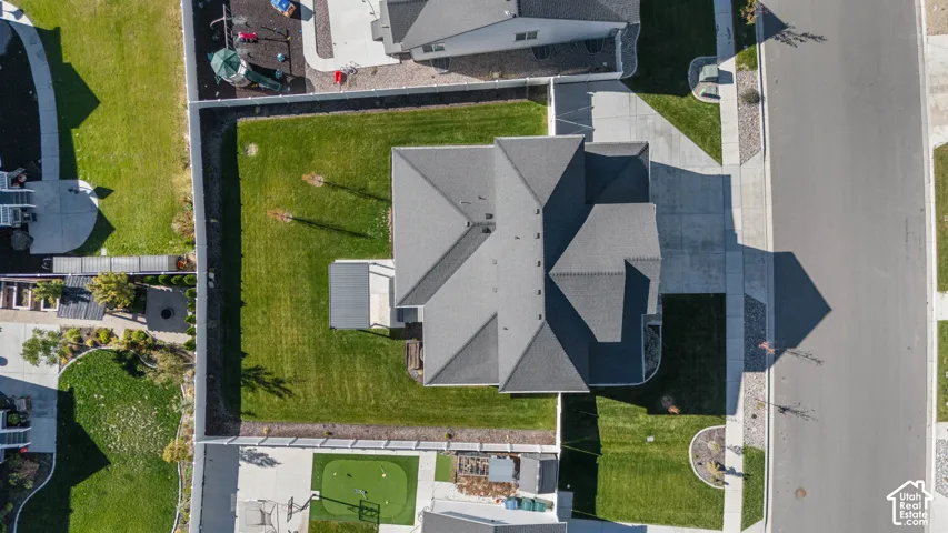 Aerial perspective of a property featuring a fenced yard, expansive lawn, concrete driveway, and covered patio