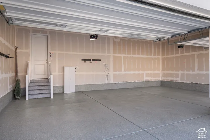 Multi-car garage featuring epoxy-coated flooring, drywall finish, and a dedicated staircase with a single-panel door