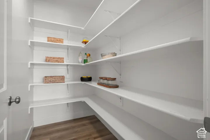 Walk-in storage space featuring multi-tiered shelving, white wall paneling, and wood-finish flooring