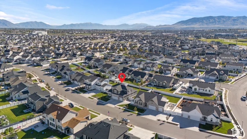 Aerial perspective of a detached residential property featuring a multi-story exterior, attached multi-car garage, fenced backyard, and surrounding mountain backdrop