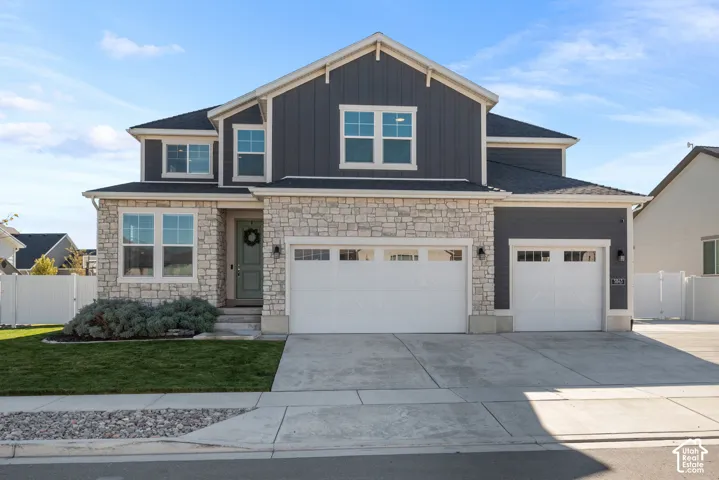 Two-story exterior featuring vertical board-and-batten siding, stone masonry accents, a three-car garage, and multi-pane windows