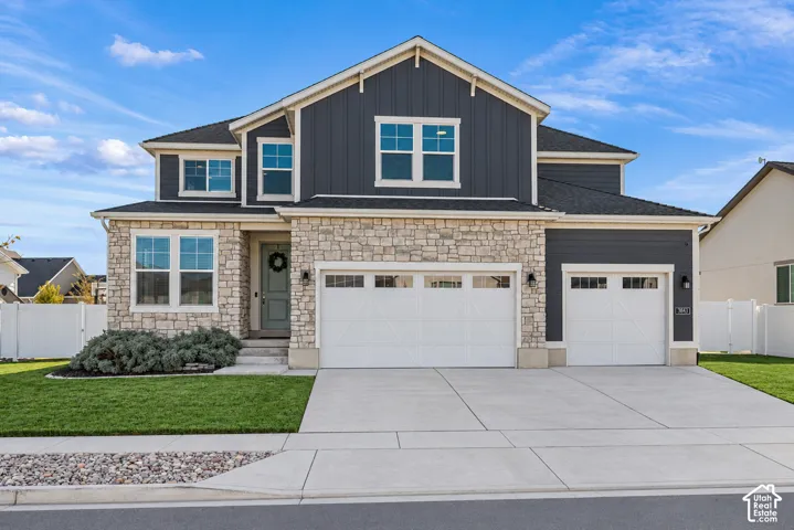 Two-story exterior featuring vertical siding, stone veneer accents, a three-car garage, and a concrete driveway