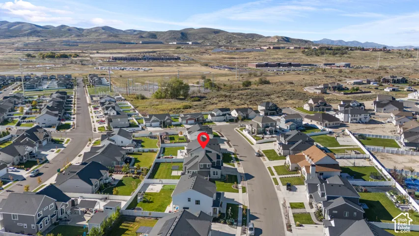 Aerial perspective of residential property featuring a multi-story exterior with a shingled roof, attached garage, fenced rear yard, and mountain backdrop