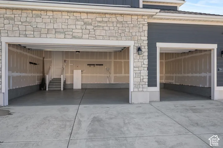 Three-car garage featuring stone veneer siding, fiber cement lap siding, concrete flooring, and interior stairway access