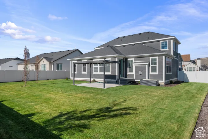 Rear exterior featuring a dark grey horizontal siding, a concrete patio with a metal pergola, a fenced backyard, and a raised metal garden bed