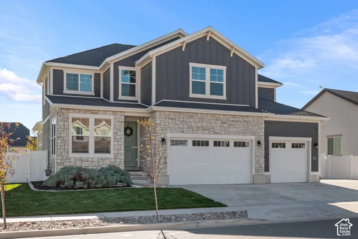 Two-story residence featuring a board-and-batten and stacked-stone exterior, multi-pane windows, a three-car garage with carriage-style doors, and a concrete driveway