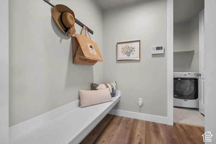 Built-in white storage bench featuring a mounted coat rack, wood-finish flooring, and a doorway entry to a laundry area with tile flooring and a built-in shelving unit