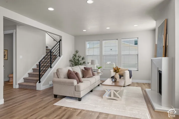 Living area featuring wood-finish flooring, recessed lighting, a fireplace with a white mantel, and a staircase with a black metal railing