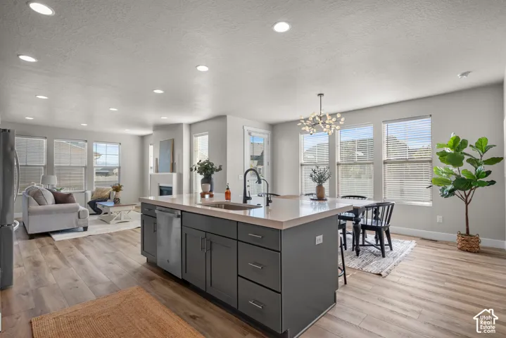 Kitchen featuring a central island with neutral solid-surface countertops, dark cabinetry, stainless steel dishwasher, recessed lighting, and wood-finish flooring