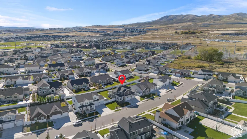 Aerial perspective of a detached residential property featuring a multi-gable roofline, exterior stone and siding accents, an attached two-car garage, and a fenced backyard, set against a mountainous horizon