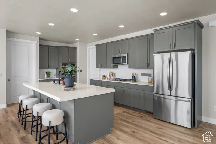 Kitchen featuring grey shaker-style cabinetry, quartz countertops, stainless steel appliances, a central island, and wood-finish flooring
