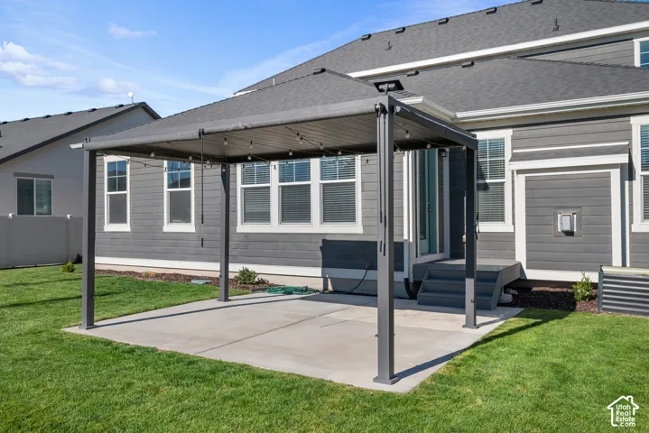 Rear exterior featuring a concrete patio, a metal-frame pergola with a retractable canopy, horizontal lap siding, and a fenced yard
