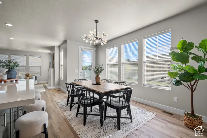 Open-concept dining area featuring wood-finish flooring, recessed lighting, a modern multi-light chandelier, and large windows with horizontal blinds