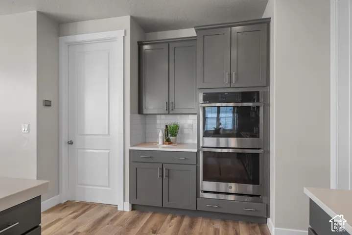 Built-in stainless steel double wall ovens, charcoal-toned shaker cabinetry, white subway tile backsplash, and wood-finish flooring
