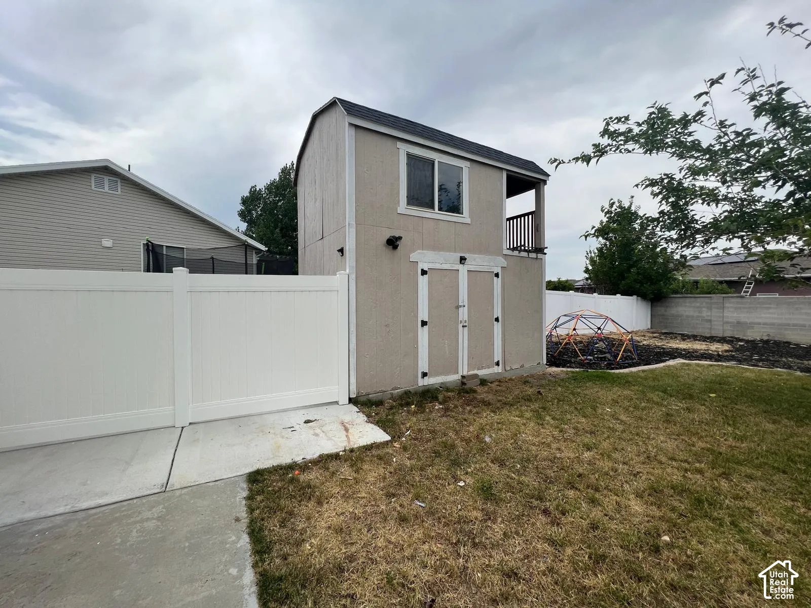 Two-story exterior storage structure featuring a balcony, double-door access, a vinyl fence, and a concrete pad