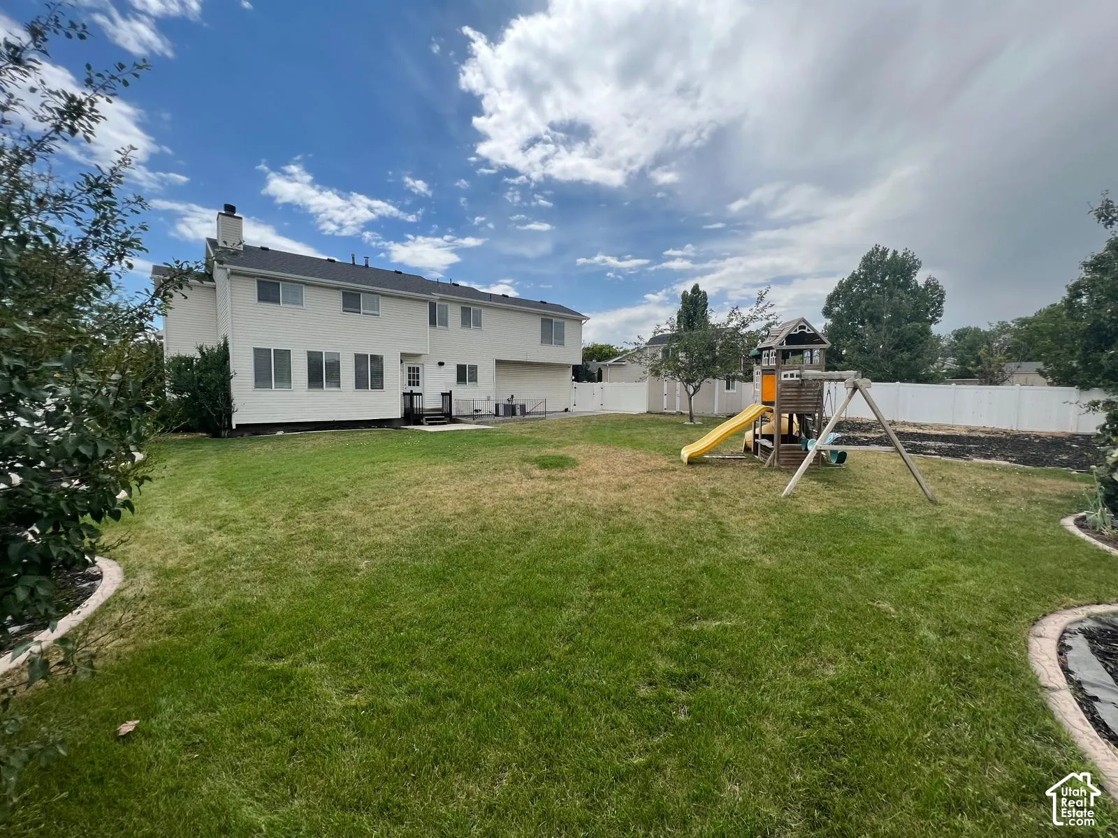 Spacious backyard featuring a large grass lawn, white perimeter fencing, and mature trees